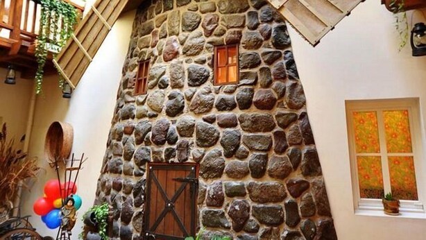A stone building with a sloped roof, a wooden door, and a window with a floral pattern. - Centro Kubas - Angel (Vilnius)