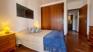 A bedroom with a bed, two bedside lamps, a wooden wardrobe, and a blue throw blanket. - Albufeira Balaia Mar e Sol (Albufeira)