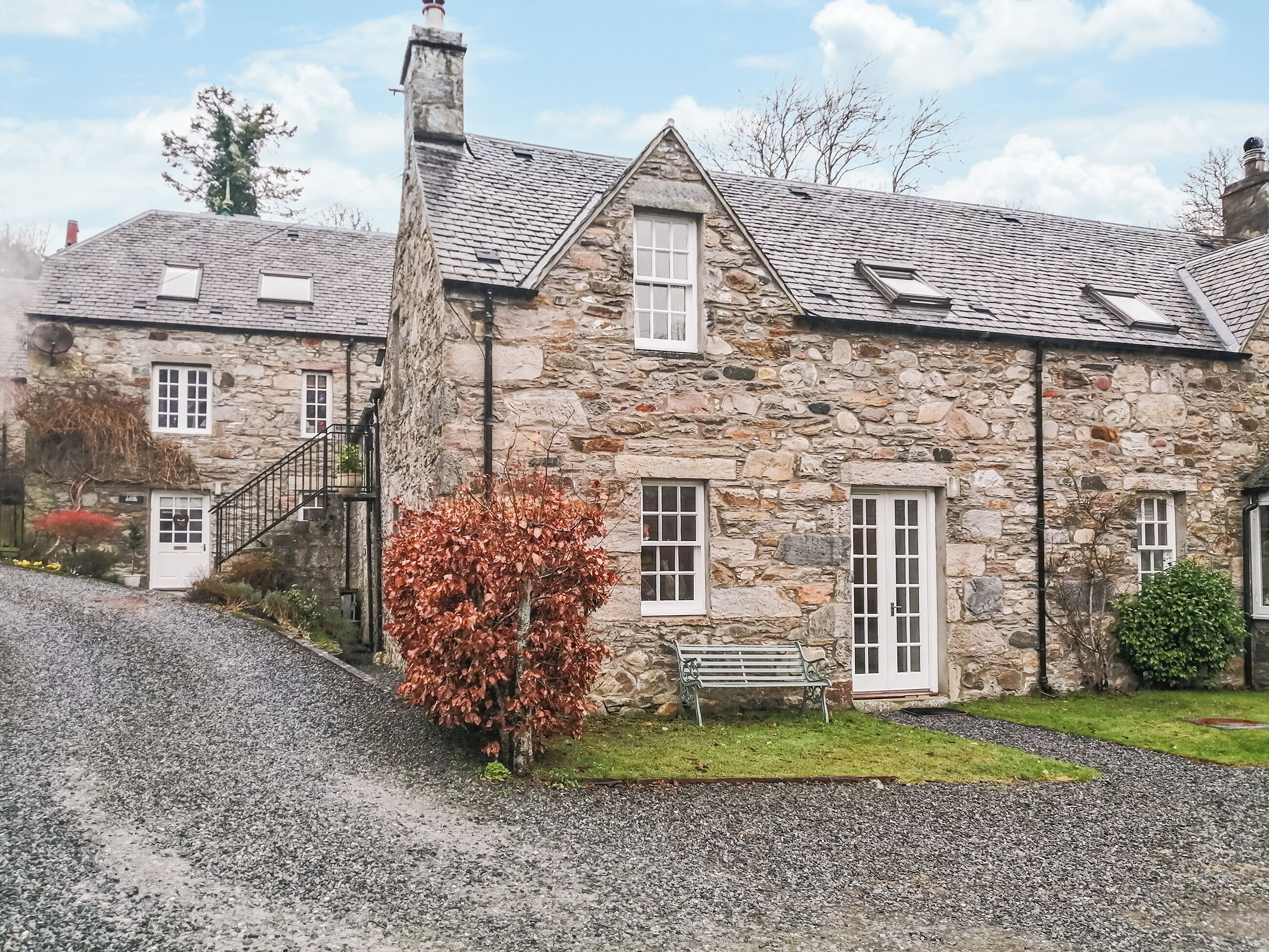 A stone house with a sloped roof, a chimney, and a small garden with a bench.