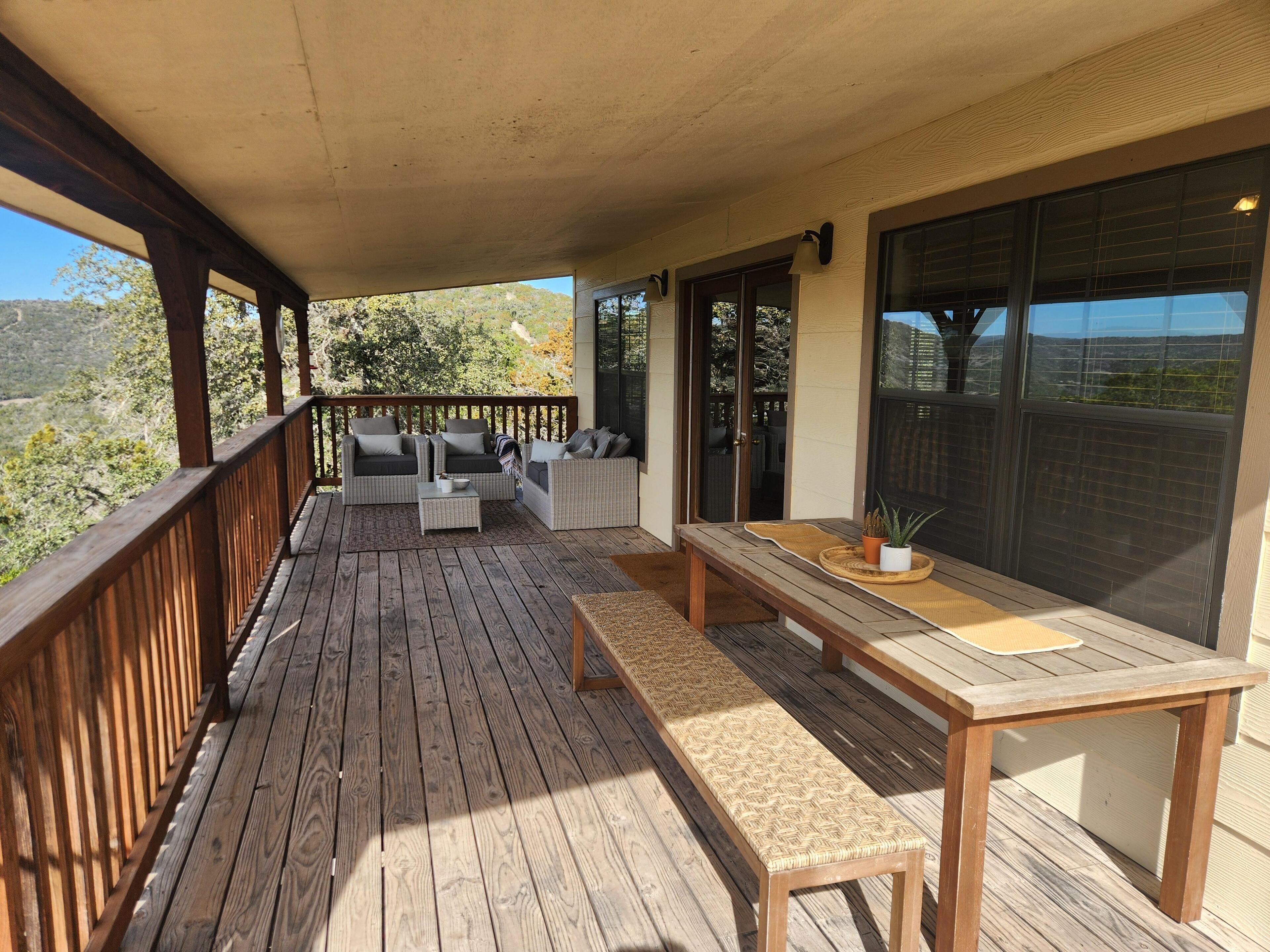 A wooden deck with outdoor furniture, including sofas and a table, overlooking a scenic landscape.