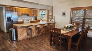 A kitchen with wooden cabinets, a stainless steel refrigerator, a bar stool area, and a dining table with chairs. - Frio Honeymoon - Best view in Concan (Concan)