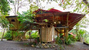 A bamboo structure with a red roof, surrounded by rocks and plants. - Bamboo Beach House Steps away from secluded beach (Provincia de Puntarenas)