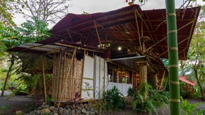 A bamboo structure with a red roof, surrounded by rocks and plants. - Bamboo Beach House Steps away from secluded beach (Provincia de Puntarenas)