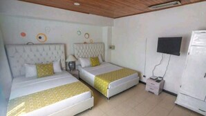 A hotel room with two beds, a television, a refrigerator, and a small table with a lamp.