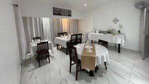 A dining area with white tablecloths, wooden chairs, and a white tiled floor. - SEMENI ASANTE GUESTHOUSE (Johannesburg South)