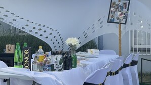 A covered outdoor event space with tables set for an event, featuring white tablecloths, chairs with black sashes, and a decorative backdrop. - SEMENI ASANTE GUESTHOUSE (Johannesburg South)