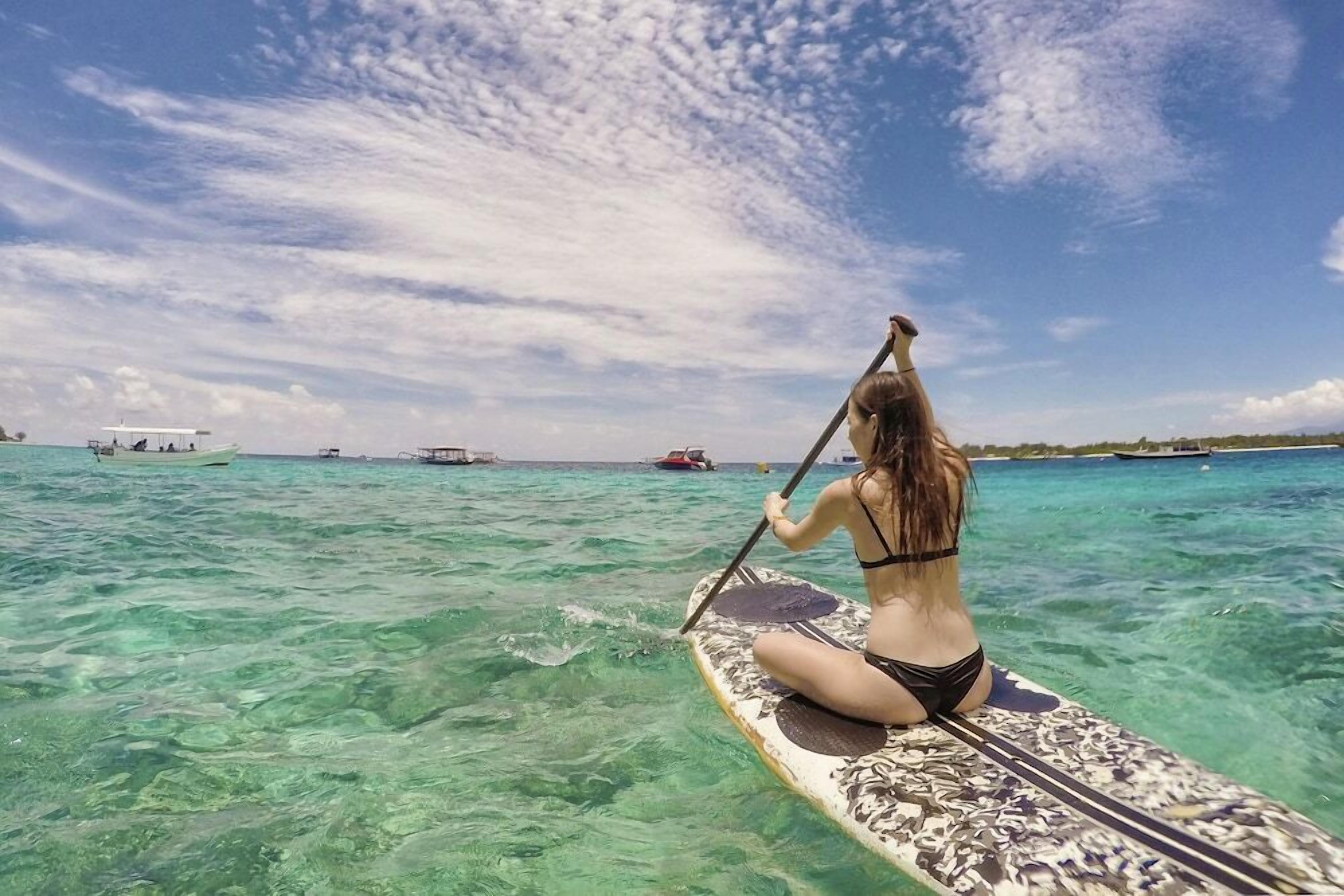 A person paddling a paddleboard in clear turquoise water.