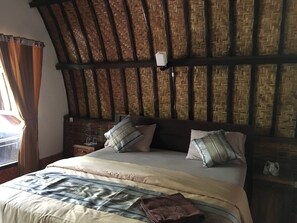 Une pièce avec un haut plafond en bois, un lit recouvert d’une couverture à rayures, deux oreillers et une table de chevet sur laquelle se trouvent des lunettes.