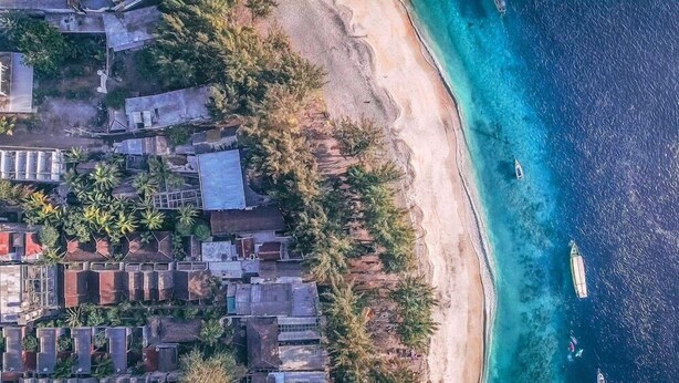Vista aérea de una zona costera con edificios, una playa de arena y aguas azules cristalinas.
