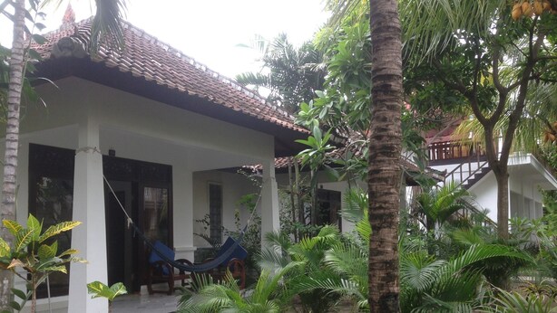 A house with a covered porch, a hammock, and lush tropical vegetation. - Warna Beach Hotel (Gili Trawangan)