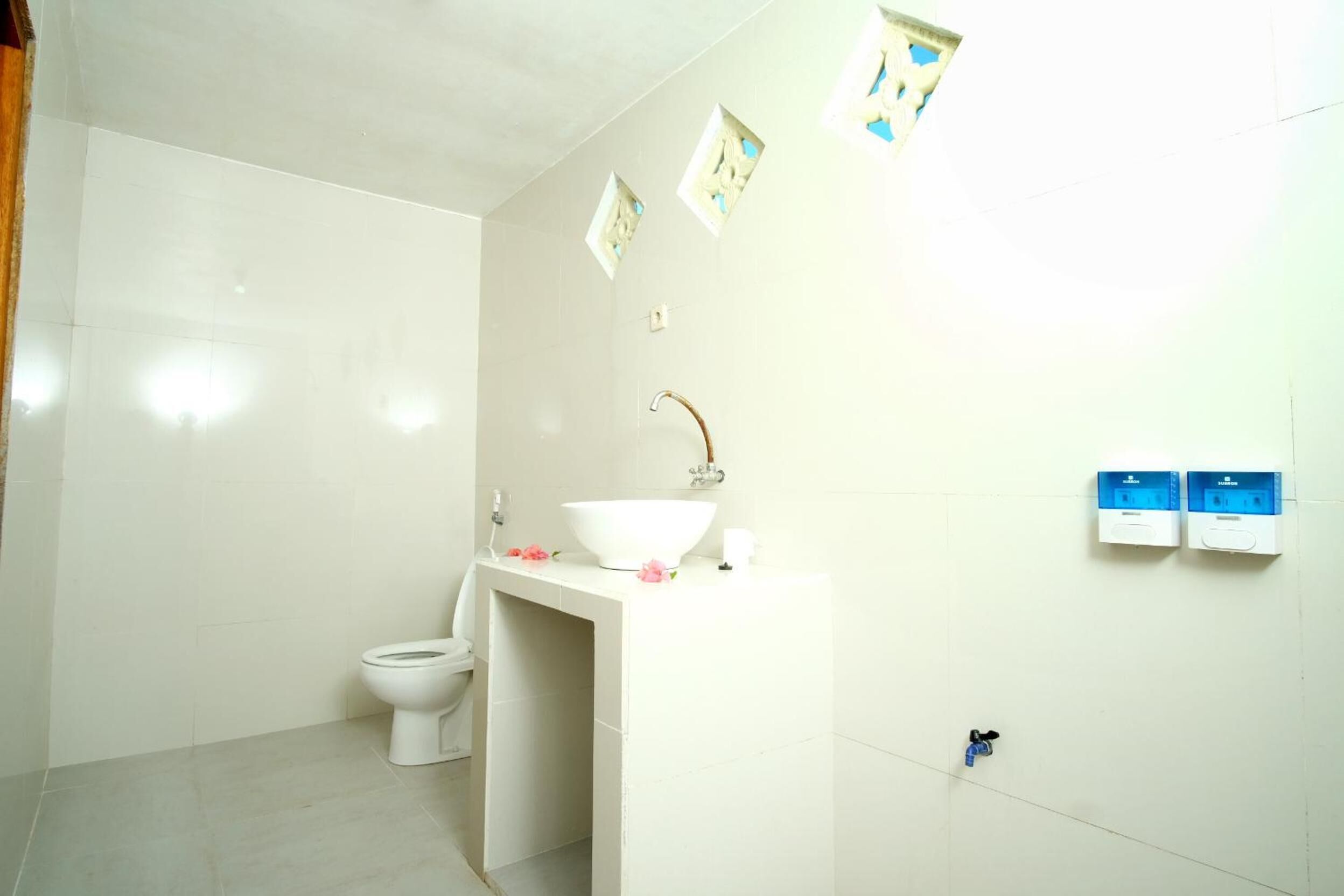 Un baño con inodoro, lavabo de porcelana blanca y dos enchufes en la pared.