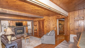 Una sala de estar acogedora con chimenea, sofá de cuero y un letrero que dice 'Welcome to our Lake House'.