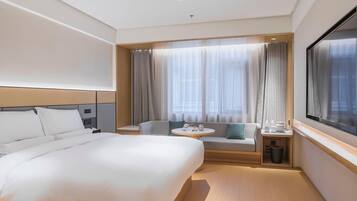 Una habitación de hotel con una cama grande, una zona de estar con una mesa y un ventanal con cortinas.