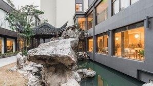 A courtyard with a rock formation, a traditional pavilion, and a modern building with large windows.