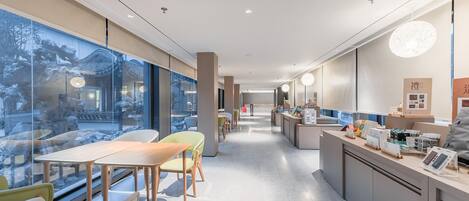 A modern hotel lobby with a long reception desk, seating area, and large windows overlooking a traditional courtyard.