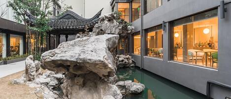 Une cour intérieure agrémentée d’une formation rocheuse, d’un pavillon de style traditionnel et d’un bâtiment moderne doté de grandes fenêtres.