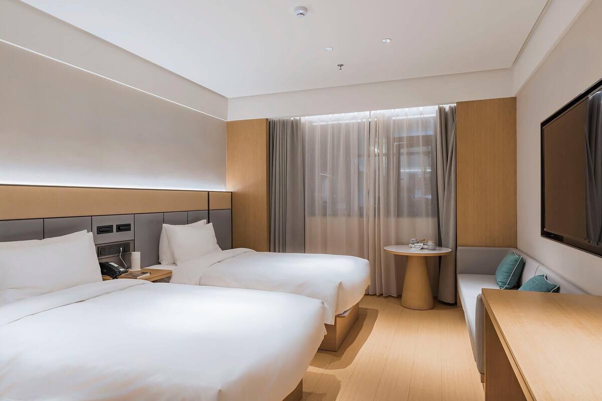 A hotel room with two beds, a small round table, a sofa, and a large TV screen.
