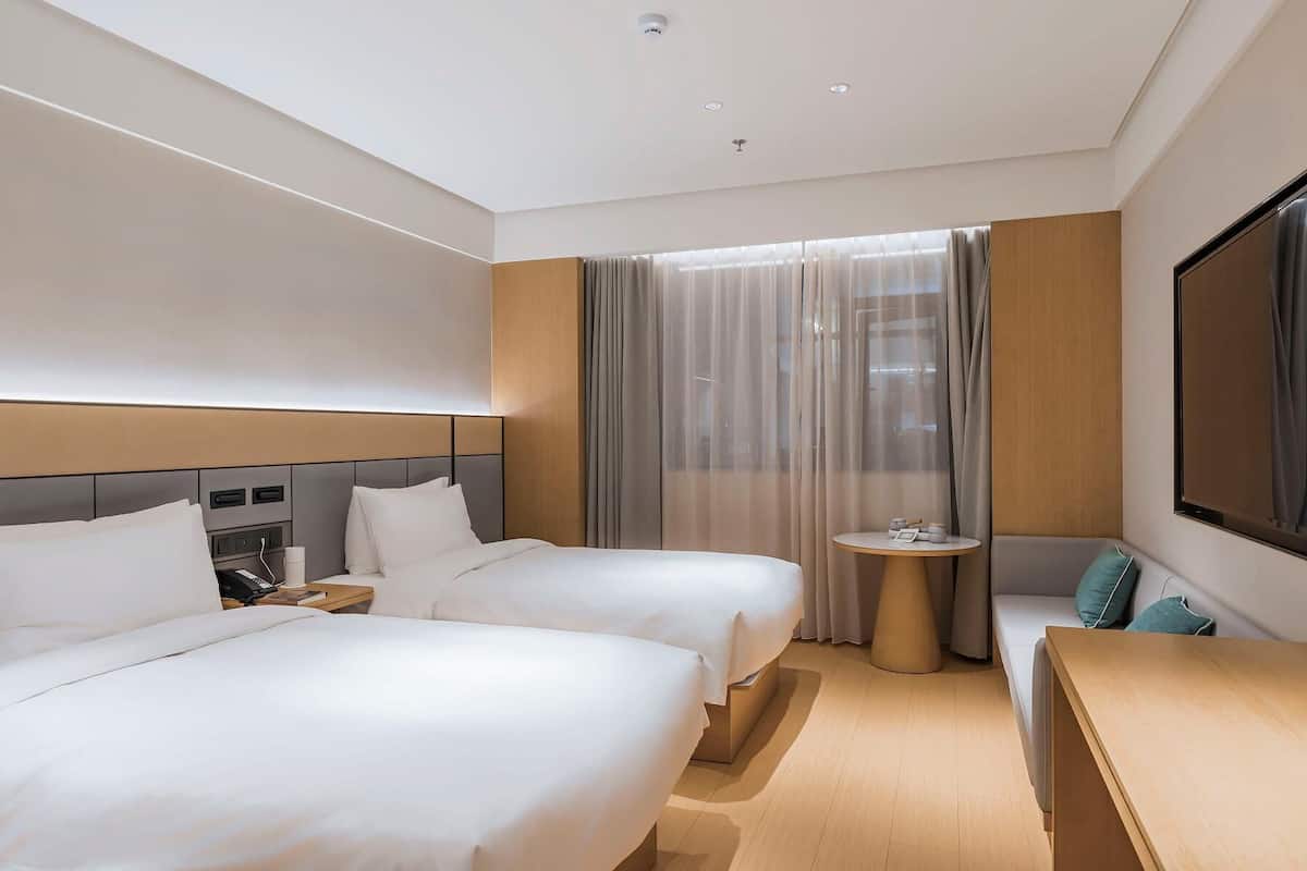 A hotel room with two beds, a small round table, a sofa, and a large TV screen.