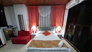 Een hotelkamer met een groot bed, twee bedlampen, een rode fauteuil en een minibar.