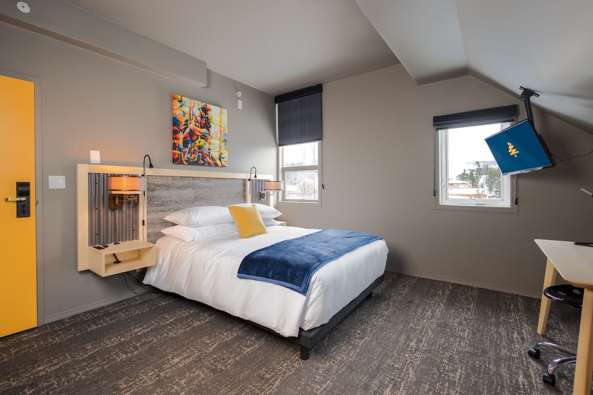 A modern bedroom with a bed, a desk, a window, and a painting on the wall.