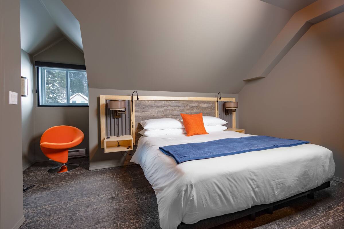 A bedroom with a bed, a chair, a window, and a sloped ceiling.