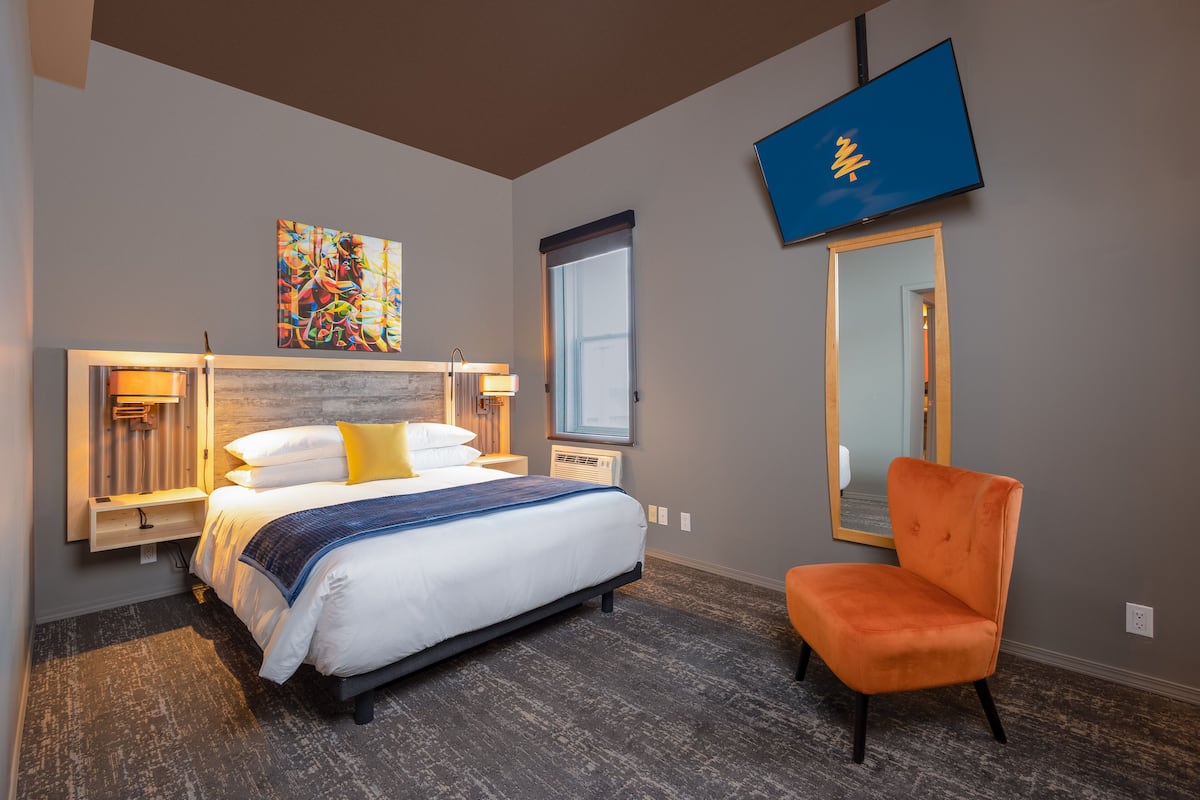 A hotel room with a bed, a chair, a TV, a window, and a painting on the wall.