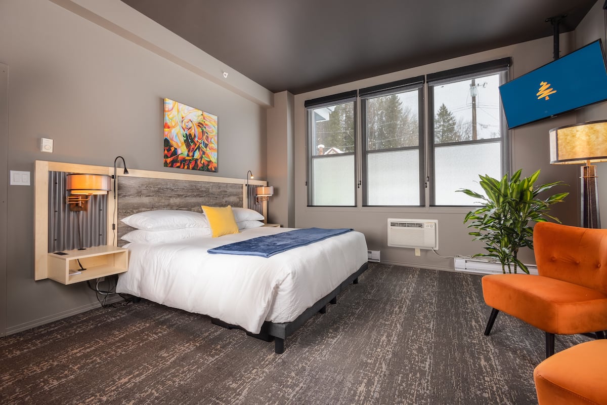A modern hotel room with a large bed, a desk, a chair, a TV, and a window with a view of trees.