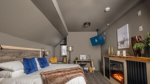 Et moderne hotelværelse med en stor seng, et skrivebord, en pejs og et ophængt fjernsyn.