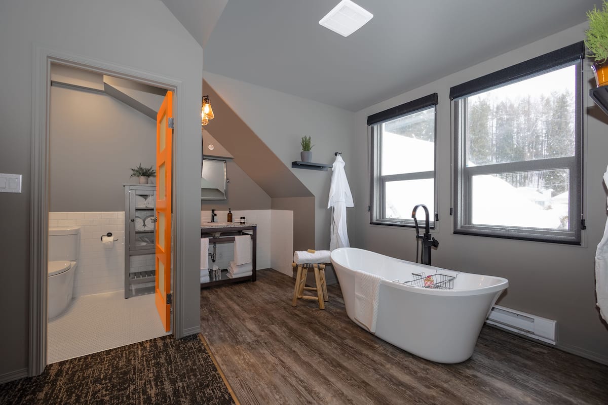 A modern bathroom with a freestanding bathtub, a wooden stool, and a towel rack.