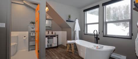 Un baño moderno con una bañera independiente, un taburete de madera y un perchero para toallas.