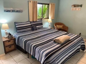 Un lit bien fait, avec une literie à rayures, une lampe de chevet, une petite table de chevet avec une lampe et une fenêtre avec des rideaux.