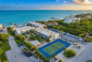 A residential area with a tennis court, parking, and a view of the ocean.