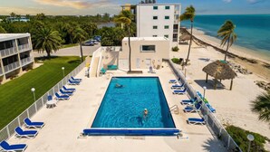 Una piscina con sillones de descanso, un edificio con balcones y vista a la playa.