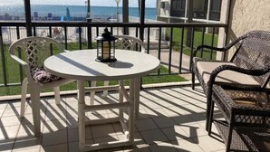 Un balcón con una mesa redonda y dos sillas, un farol y vista al océano y palmeras.