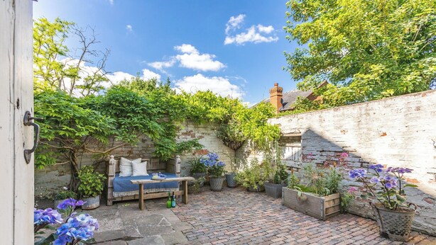 A cozy outdoor patio with a rustic stone floor, a wooden table with a blue tablecloth, and potted plants. - 2 bedroom accommodation in Tenbury Wells (Tenbury Wells)