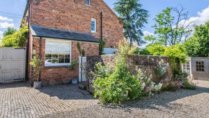 A brick house with a large window, a garden with various plants, and a gravel driveway. - 2 bedroom accommodation in Tenbury Wells (Tenbury Wells)