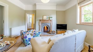 A living room with a fireplace, sofa, television, and a floral ottoman. - 2 bedroom accommodation in Tenbury Wells (Tenbury Wells)