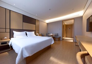 A modern hotel room with a large bed, bedside tables, a desk, and a seating area. - Ji Hotel (Yancheng)
