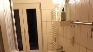 Une petite salle de bain compacte, équipée de toilettes, d’un lavabo et d’une baignoire. Une fenêtre se trouve au-dessus des toilettes et un porte-serviettes au-dessus du lavabo.