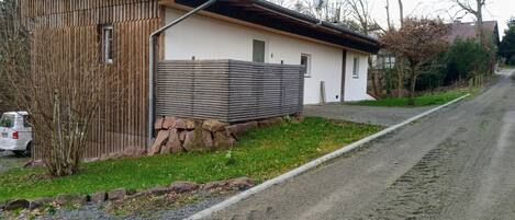 A single-story building with a sloped roof, a stone foundation, and a wooden fence.