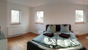 Une chambre à coucher comprenant un lit, deux tables de chevet, une lampe sur pied et deux fenêtres.