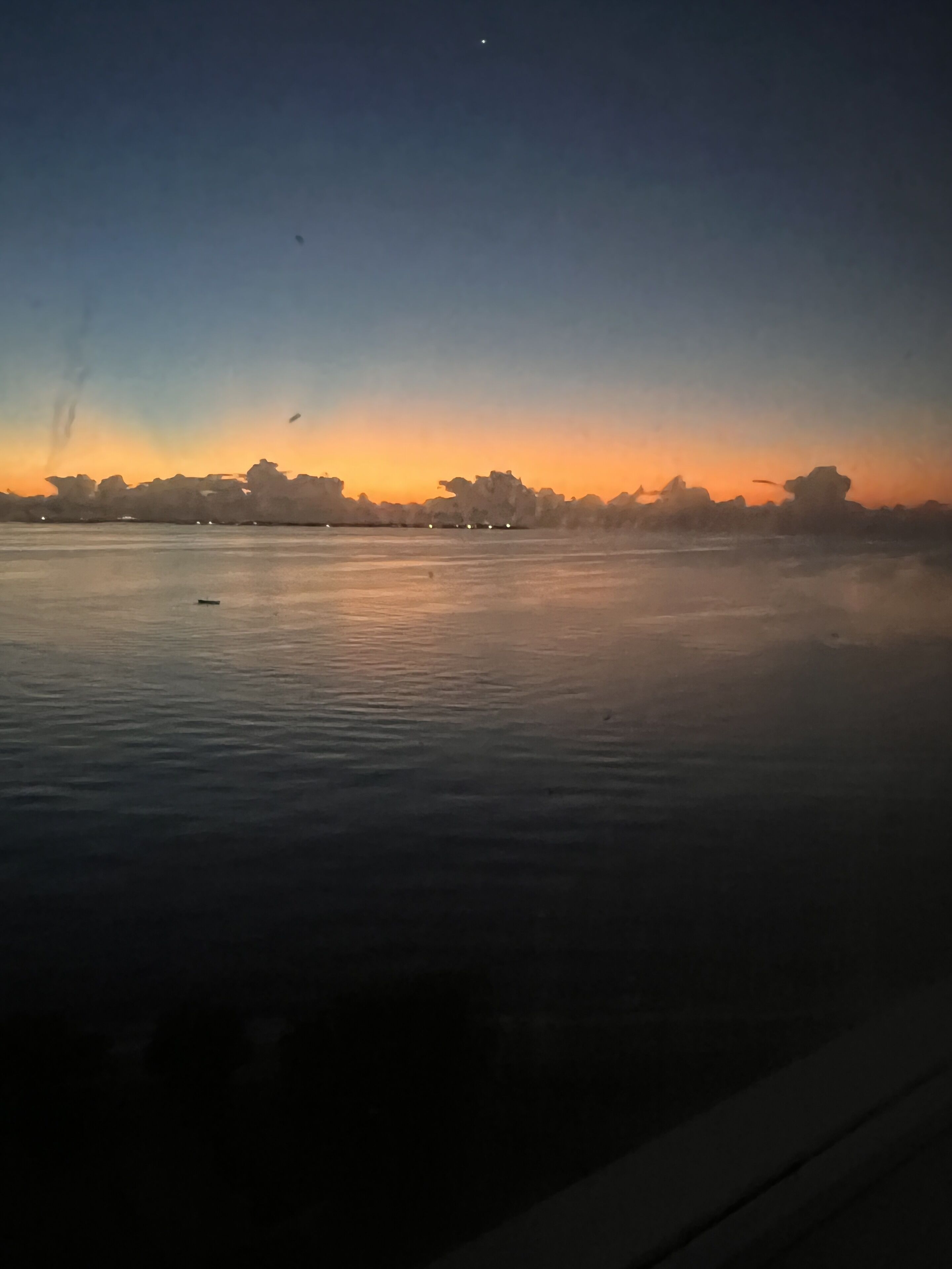 A calm body of water with a sunset in the background and silhouettes of trees.
