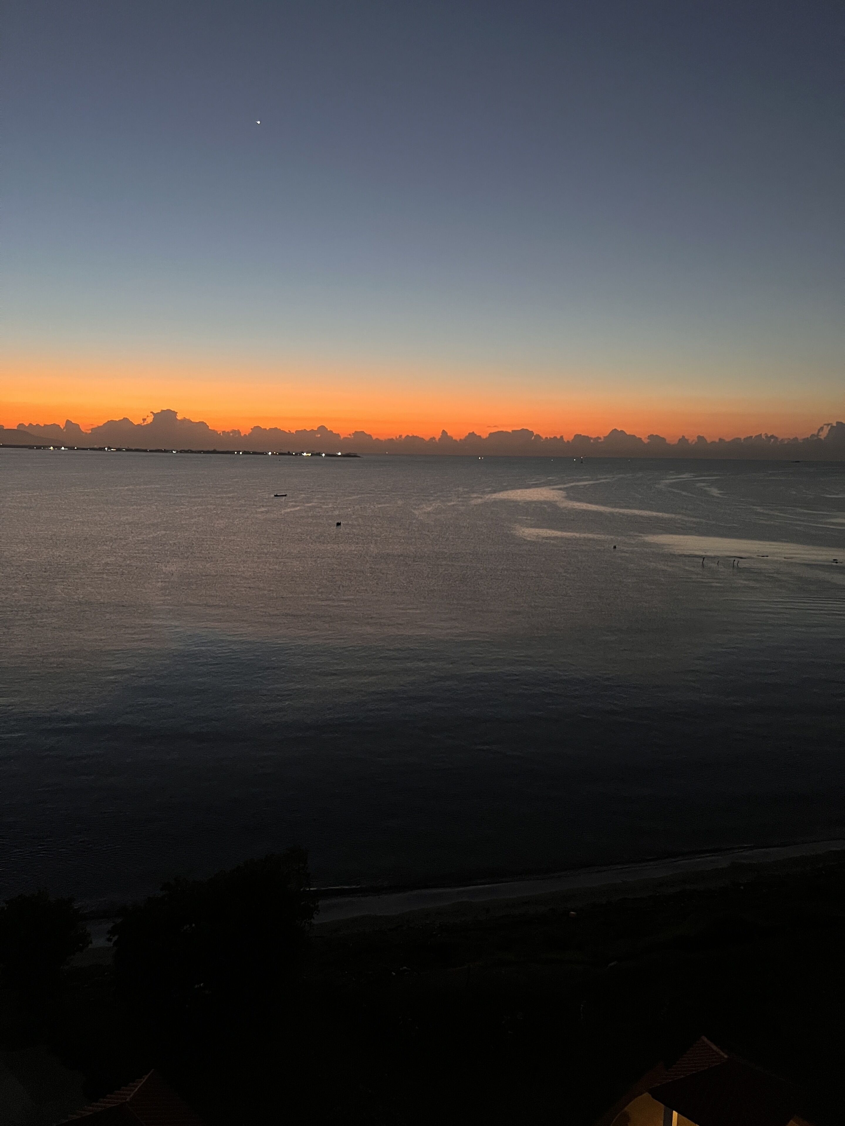 Une vue sur la côte, avec une mer calme, les contours d’une ville lointaine et un ciel dégagé.