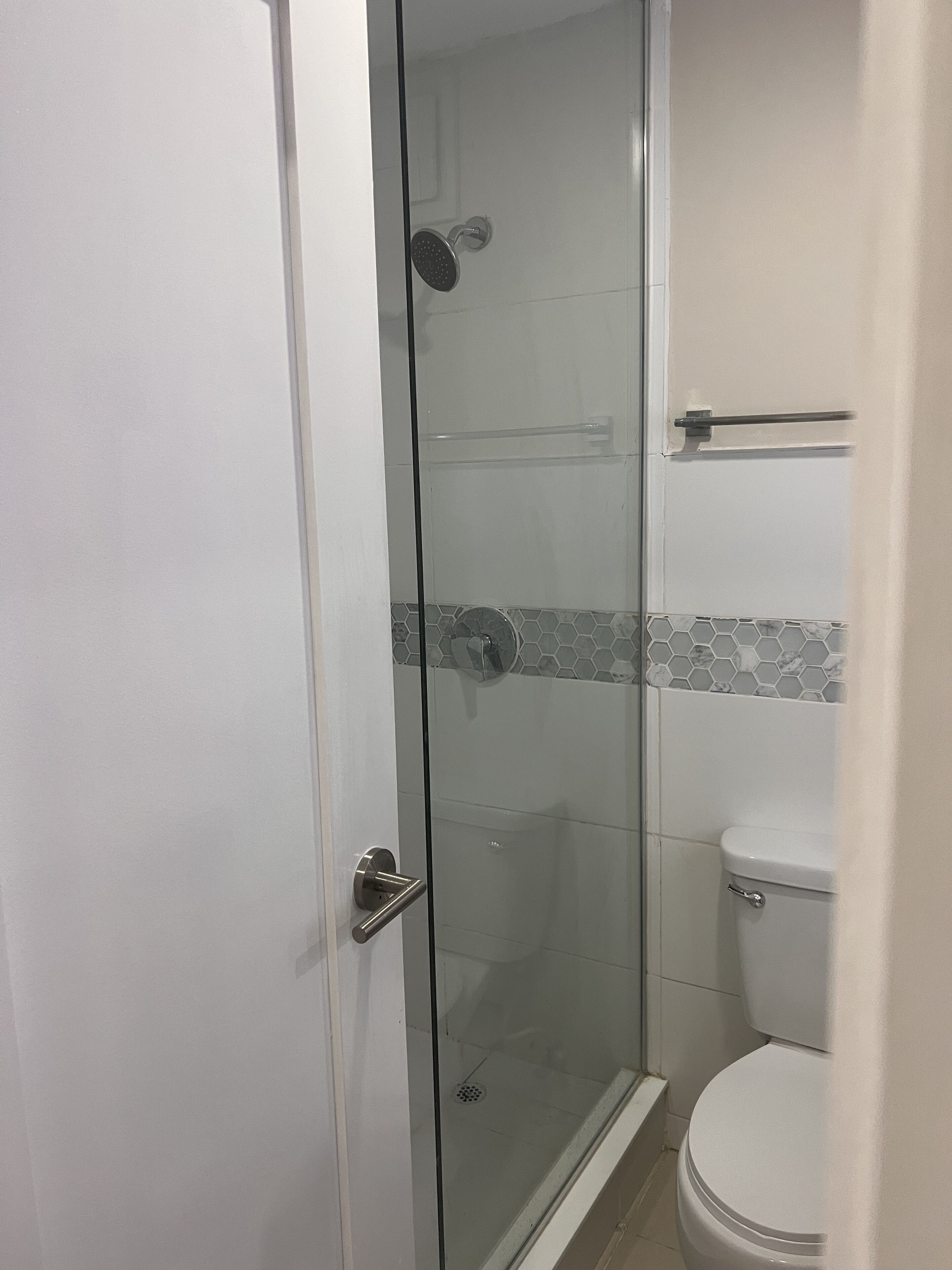 Une douche fermée par des parois de verre, avec des toilettes blanches et un porte-serviettes.