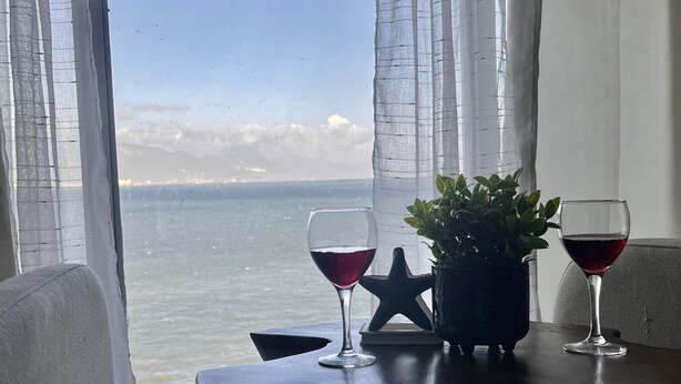 A table with two wine glasses and a star decoration, positioned near a window overlooking a body of water. - Sea Salt escape/ Beachfront apartment (Portmore)