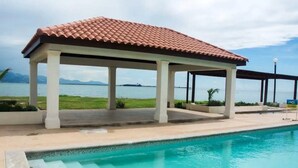 A covered pool area with a view of a body of water and mountains in the background. - Sea Salt escape/ Beachfront apartment (Portmore)