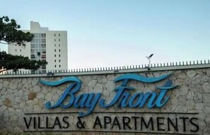 A sign for Bay Front Villas & Apartments with a stone wall and a tall building in the background. - Sea Salt escape/ Beachfront apartment (Portmore)