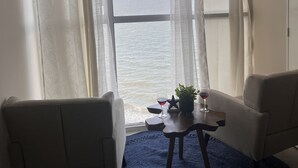 A room with a view of the sea, featuring two chairs, a small table with a glass of wine, and a potted plant. - Sea Salt escape/ Beachfront apartment (Portmore)