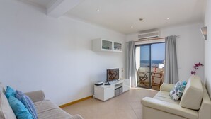 Ett modernt vardagsrum med en soffa, en tv och en balkong med utsikt över havet.