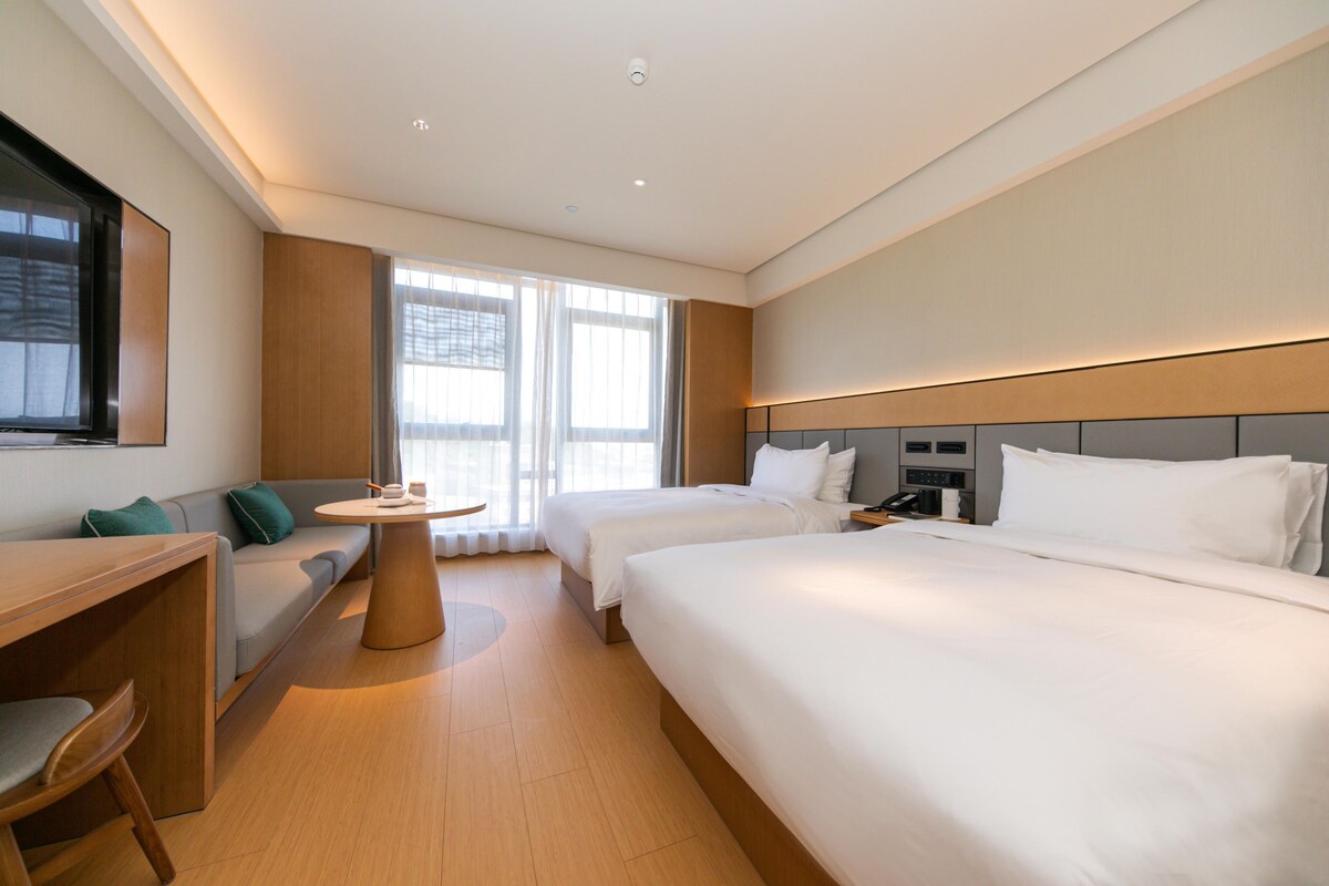 A hotel room with two beds, a desk, a chair, and a small table.